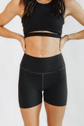 Woman wearing the black Embodie Renew Short, shown from the front with its high-rise supportive waistband.