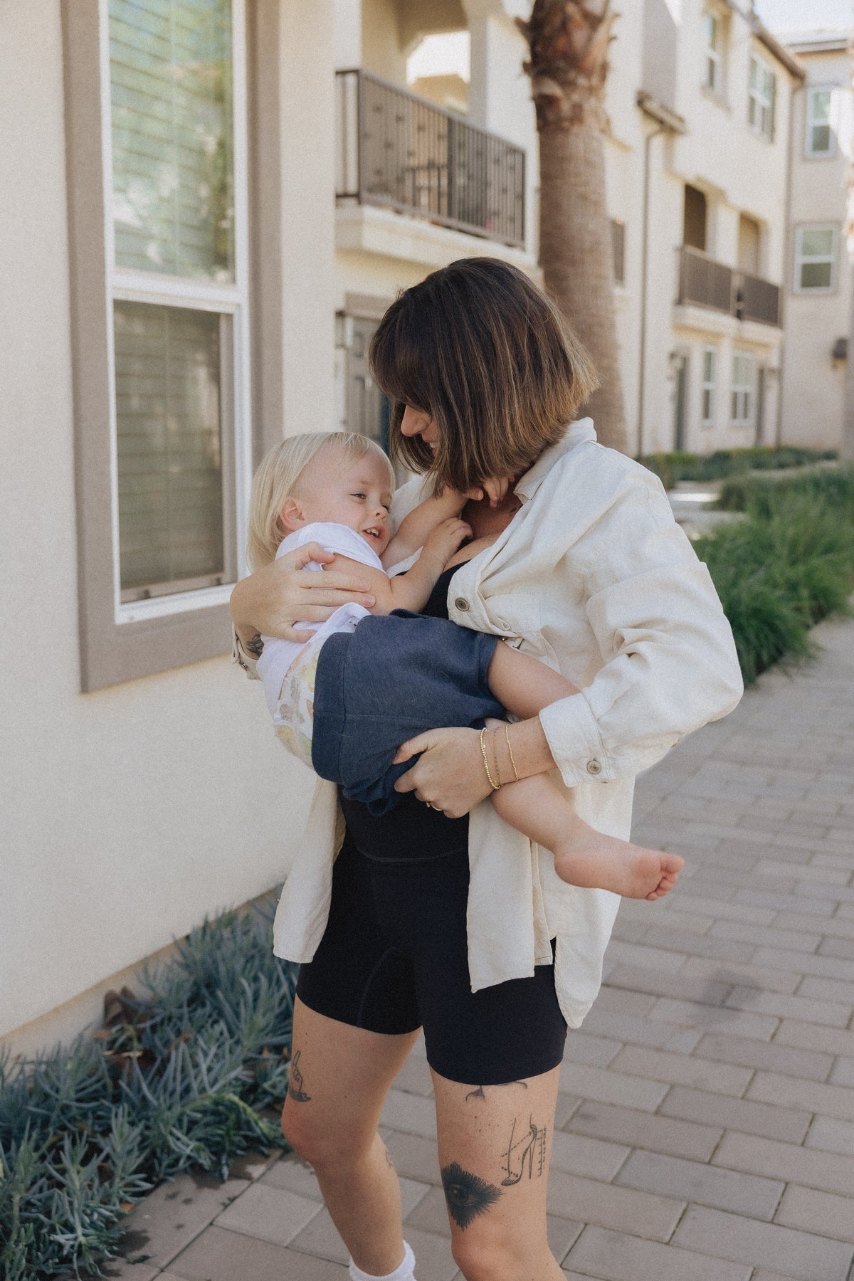 Woman wearing the black Embodie Renew Short while holding her child outdoors.